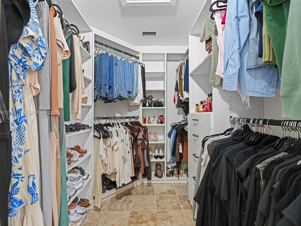 Walk-in closet featuring white built-in shelving, multiple hanging rods, integrated drawer storage, and tile flooring