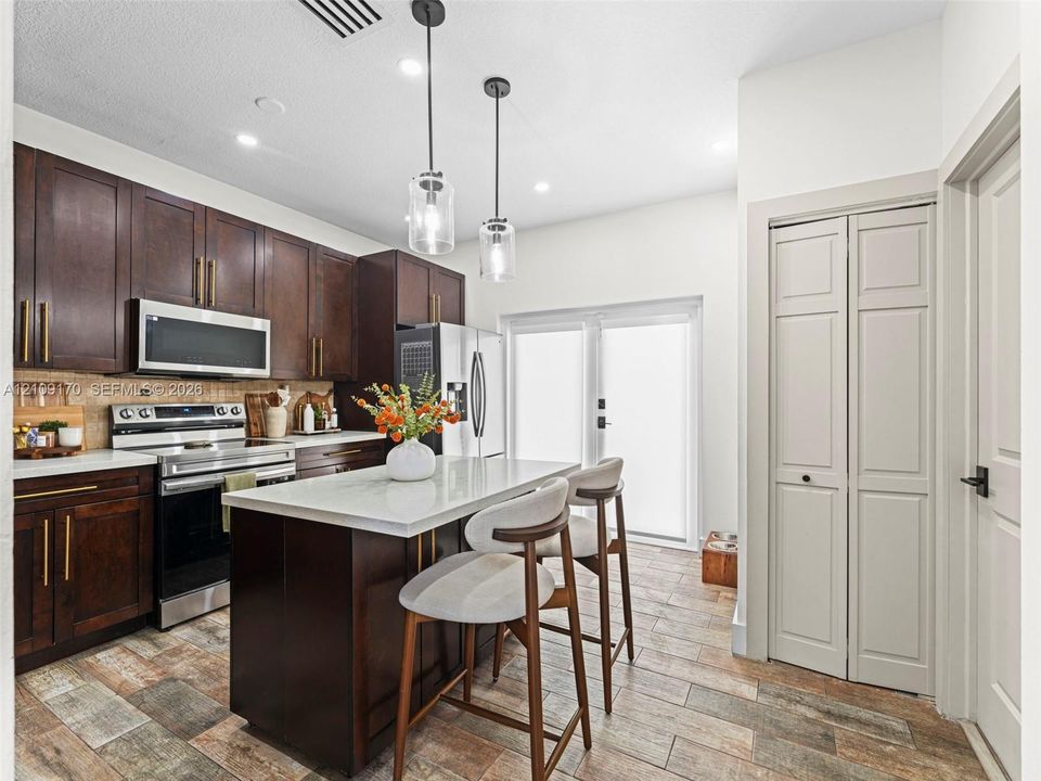 Kitchen featuring dark wood cabinetry, a central island with a stone-surface countertop, stainless steel appliances, dual glass pendant lights, and wood-finish tile flooring