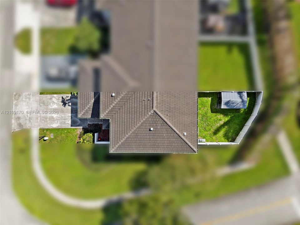 Aerial view of property featuring a concrete driveway, multi-faceted hip roof, fenced backyard, and exterior storage shed