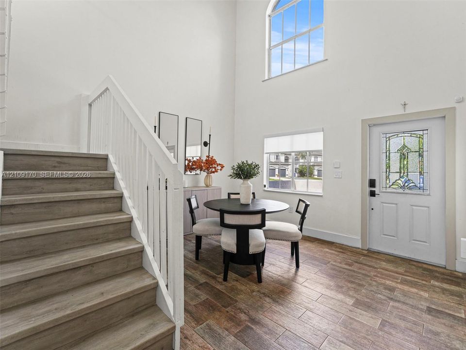 Double-height ceiling, arched window, wood-finish flooring, staircase with white railing, and exterior door with decorative glass inlay