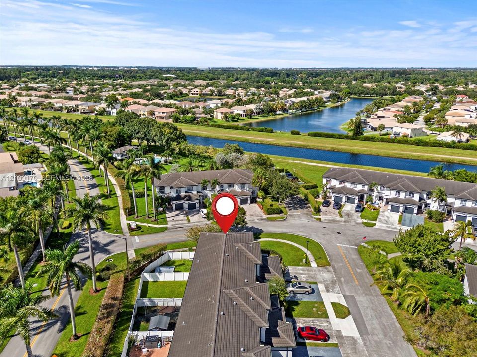 Aerial perspective of multi-family residences featuring tile roofing, private fenced yard areas, and paved driveways within a suburban community