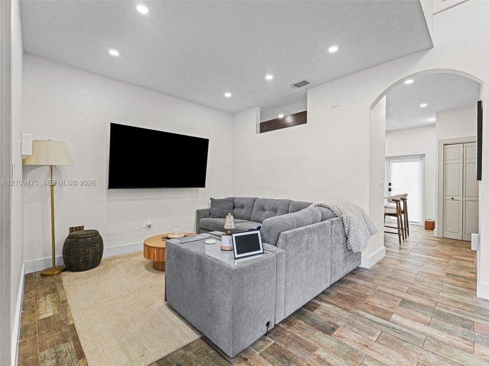 Living area featuring wood-finish tile flooring, recessed lighting, and a prominent arched entryway