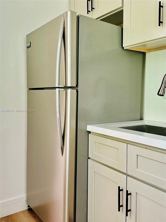 Stainless steel top-freezer refrigerator, Shaker-style cabinetry with matte black hardware, and solid-surface countertop with integrated basin