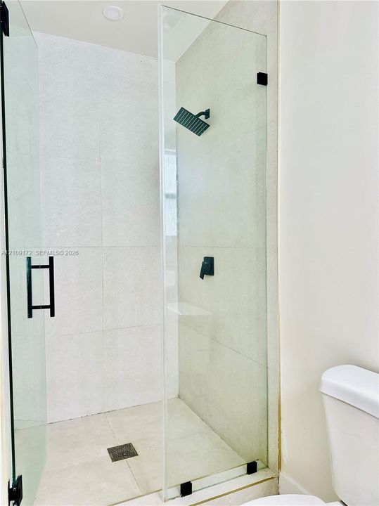 Walk-in shower featuring large-format tile surround, frameless glass enclosure, and matte black rainfall showerhead with matching hardware