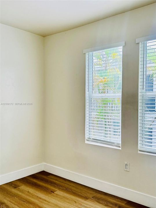 Interior space featuring wood-finish flooring, neutral wall tones, and dual windows equipped with horizontal blinds