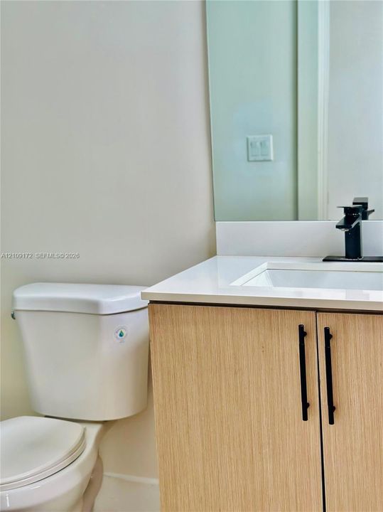 Light wood-finish vanity with a white countertop, rectangular undermount sink, matte black hardware, and a single-handle faucet