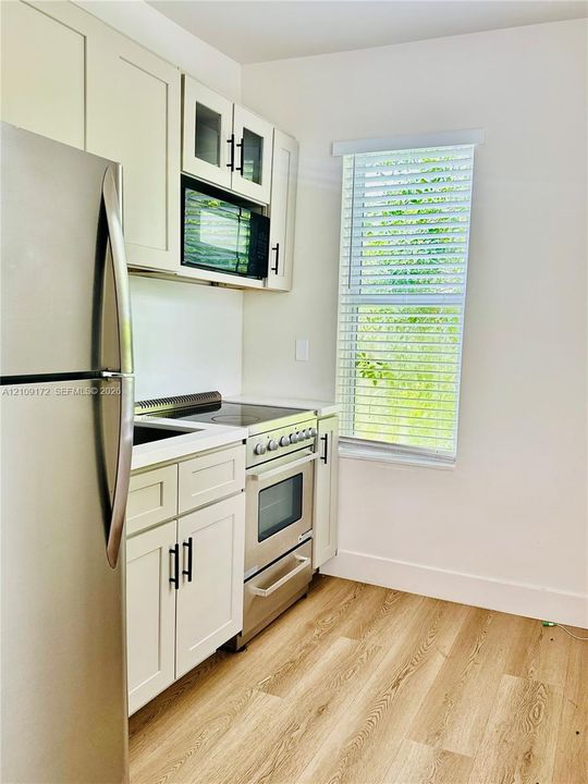 Kitchen featuring shaker-style cabinetry with matte black hardware, stainless steel appliances, wood-finish flooring, and a window with horizontal blinds