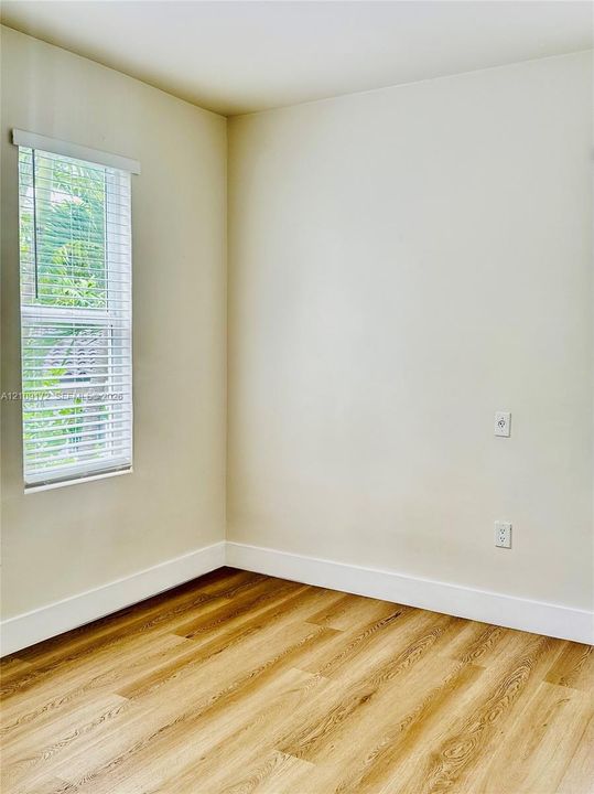 Neutral-toned interior space featuring wood-finish flooring and a single-hung window with fitted horizontal blinds