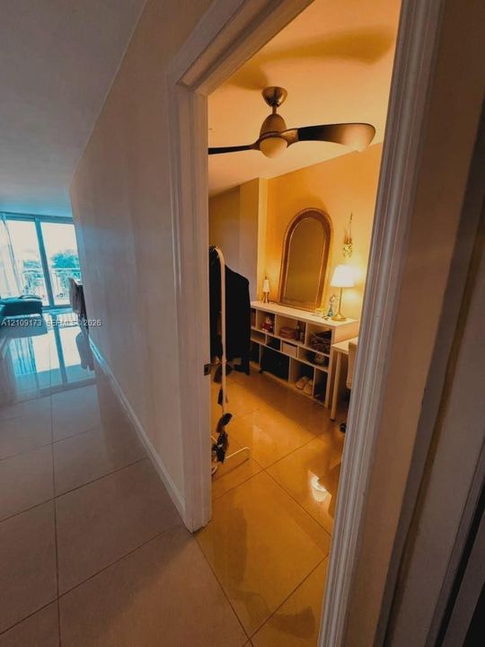 Large-format neutral tile flooring throughout, ceiling fan with matte finish, and glass-paneled sliding balcony door