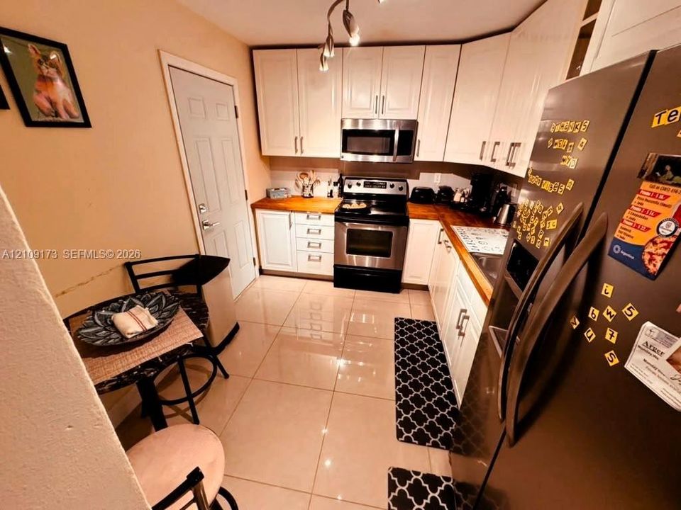 Kitchen featuring white shaker-style cabinetry, wood-finish countertops, stainless steel appliances, and large-format tile flooring