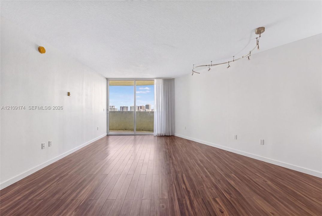 Open-concept room featuring wood-finish flooring, adjustable track lighting, and a large sliding glass door with a balcony