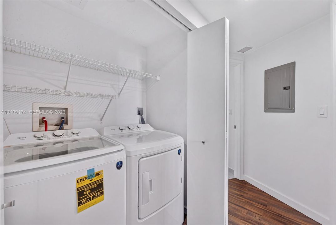 Laundry space featuring wood-finish flooring, white walls, and built-in white wire shelving