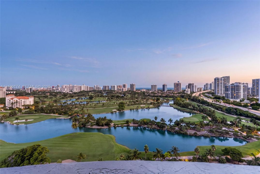 Elevated perspective featuring expansive golf course fairways, interconnected water features, mature landscaping, and a panoramic city skyline