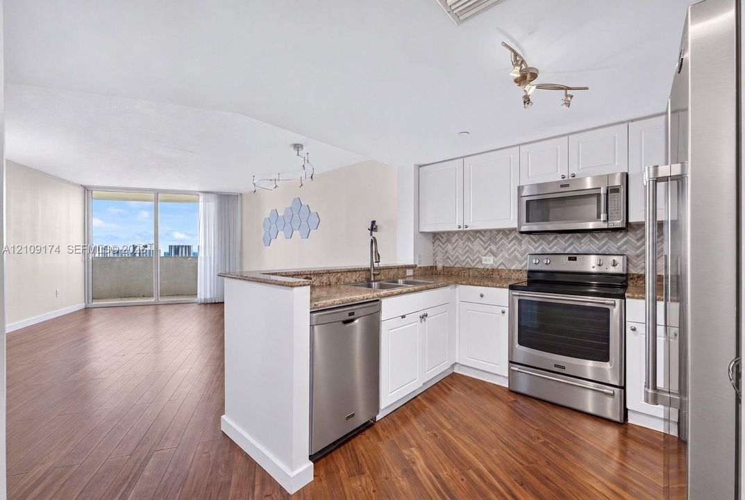 Kitchen featuring white cabinetry, stone-surface countertops, a herringbone-pattern tile backsplash, and stainless steel appliances, all set atop wood-finish flooring