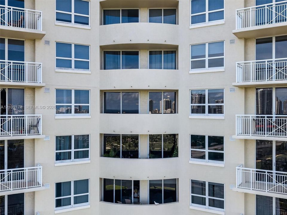 Multi-story high-rise exterior featuring a symmetrical facade, stucco finish, large glass windows, and private balconies with white railings