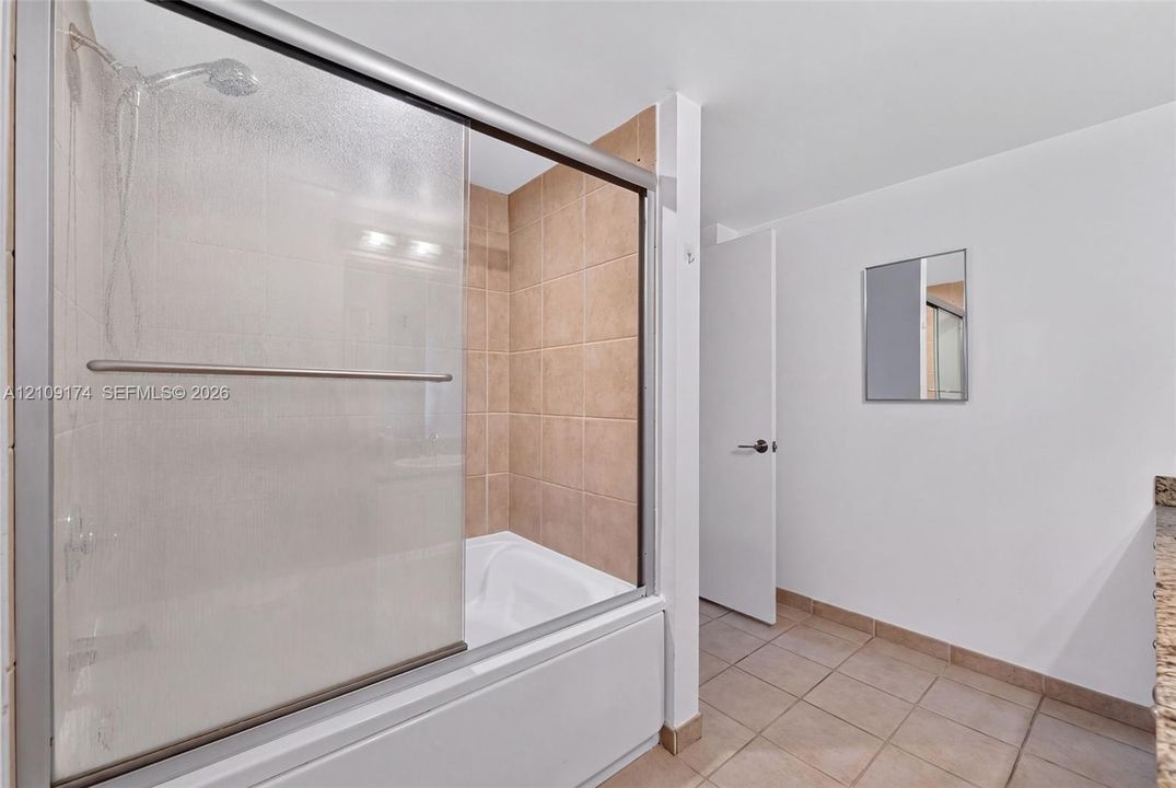 Bathroom featuring a tub-shower combination with sliding glass doors, neutral tile surround, and tiled flooring