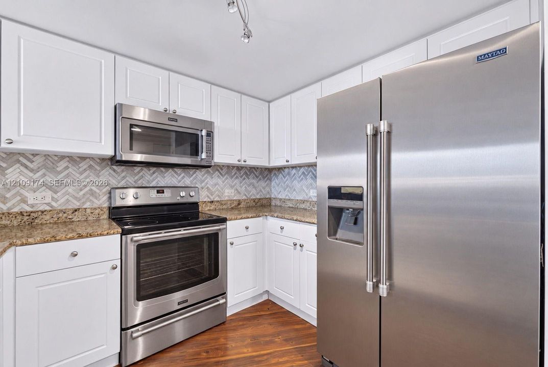 Kitchen featuring stainless steel appliances, white cabinetry, stone-finish countertops, and a herringbone-patterned tile backsplash