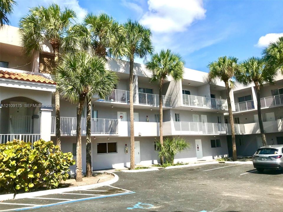 Stucco exterior featuring multi-level balconies with white metal railings, tile roof accents, and mature palm trees