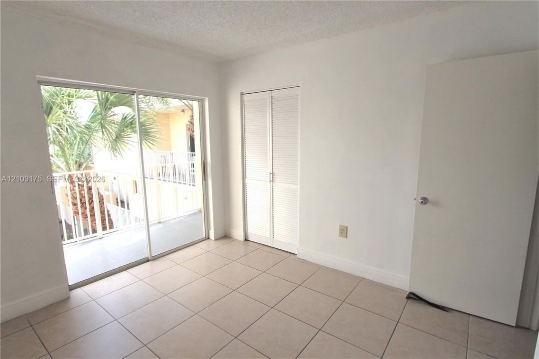 Neutral-toned floor tiles, sliding glass balcony doors, and built-in closet with louvered doors