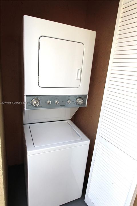 Stacked white washer and dryer unit with a top-loading basin and white louvered enclosure doors