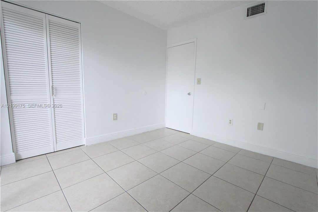 Neutral-toned tile flooring, white louvered-door closet, and solid core interior door