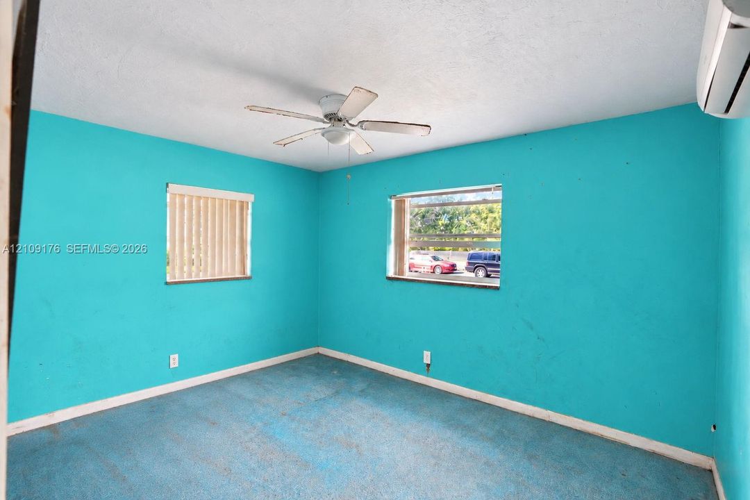 Interior room featuring two windows, a ceiling fan with light fixture, and a wall-mounted ductless air conditioning unit