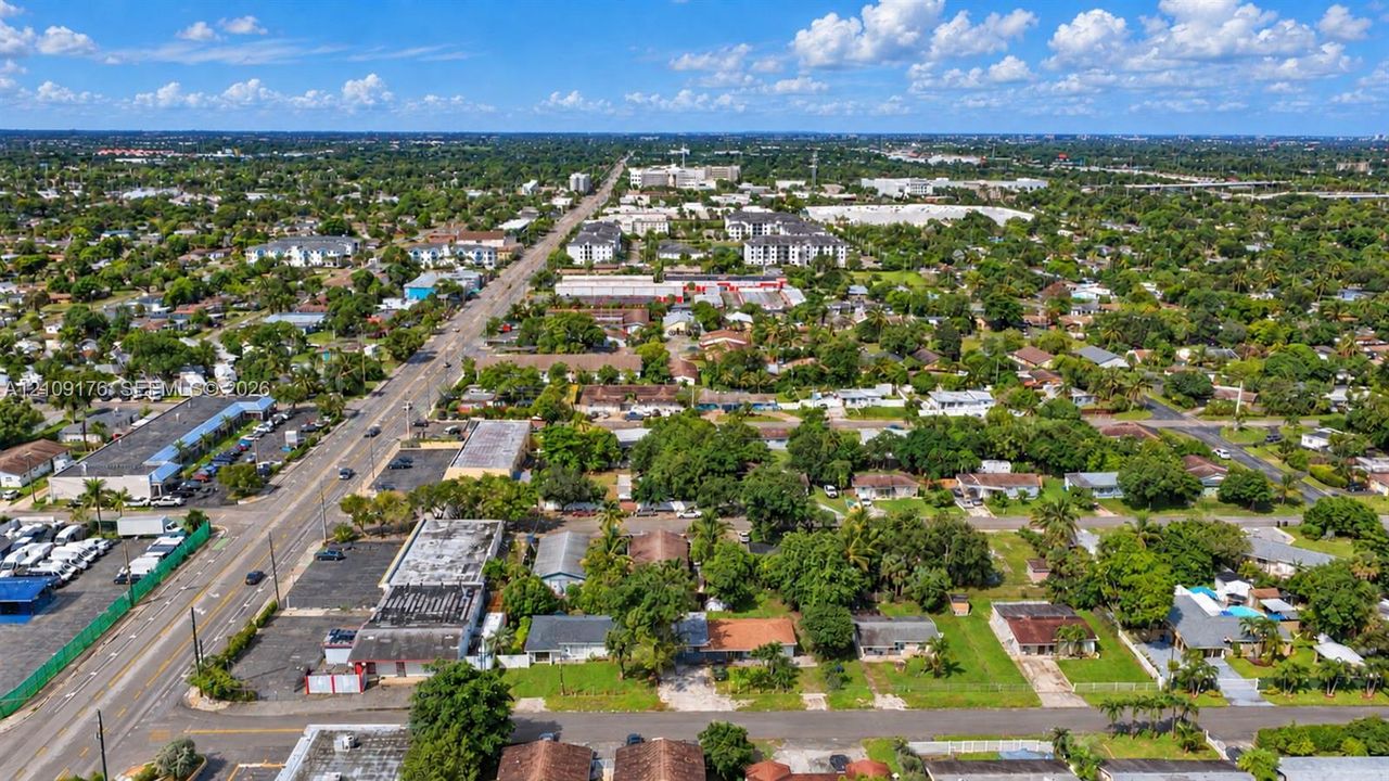 Aerial perspective of an urban setting featuring paved thoroughfares, established residential blocks, mature tree canopy, and access to commercial infrastructure