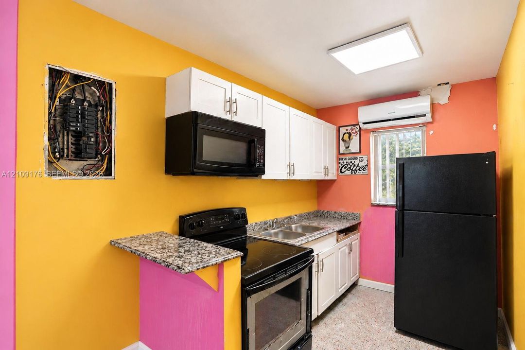 Kitchen featuring white cabinetry, stone-finish countertops, stainless steel sink, black range with over-the-range microwave, and wall-mounted climate control unit