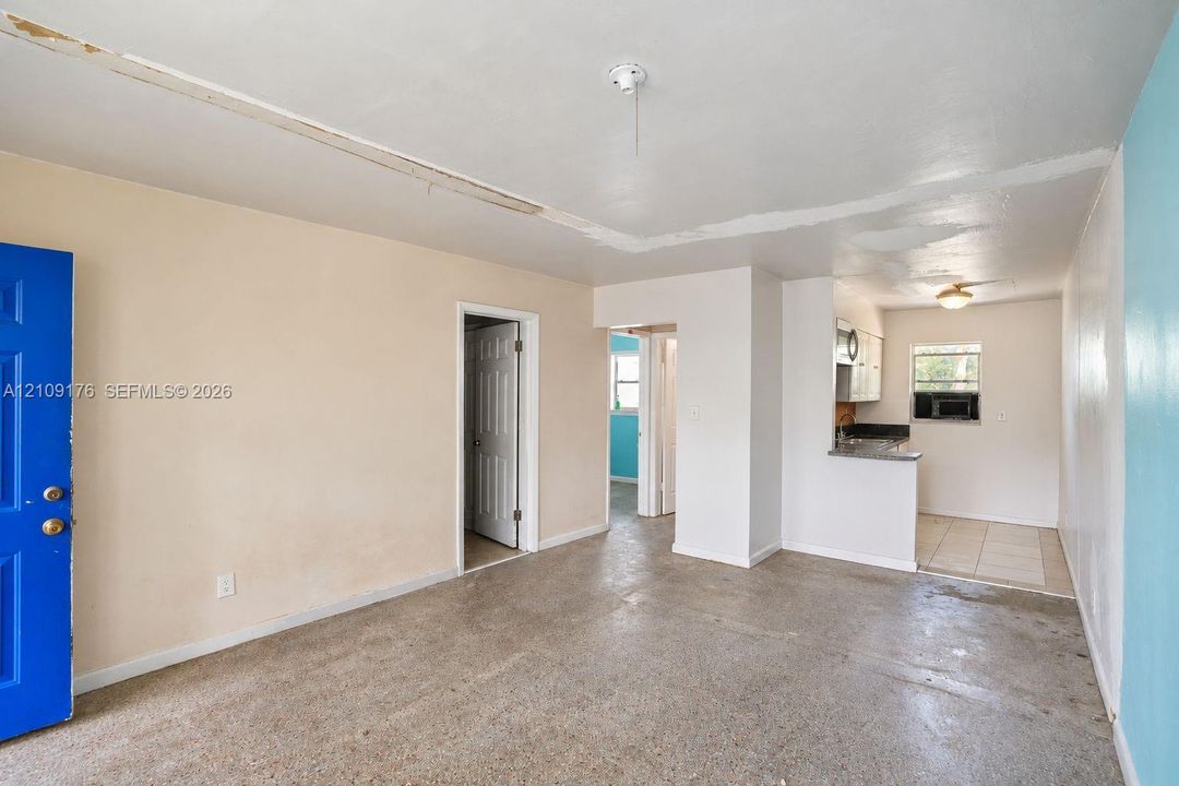 Interior featuring polished concrete flooring, white ceiling-mounted light fixtures, multi-panel doors, and an open-concept kitchen area with stone-finish countertops and cabinetry