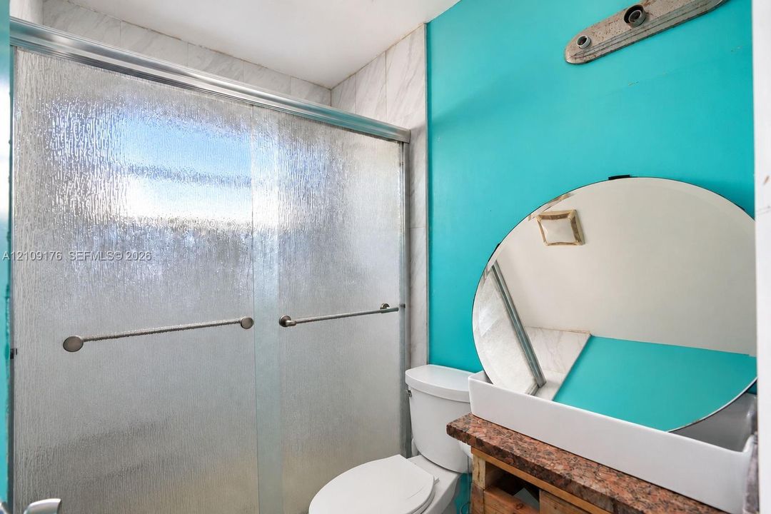 Bathroom featuring a glass shower enclosure with textured panels, a circular wall mirror, and a stone-surface vanity countertop