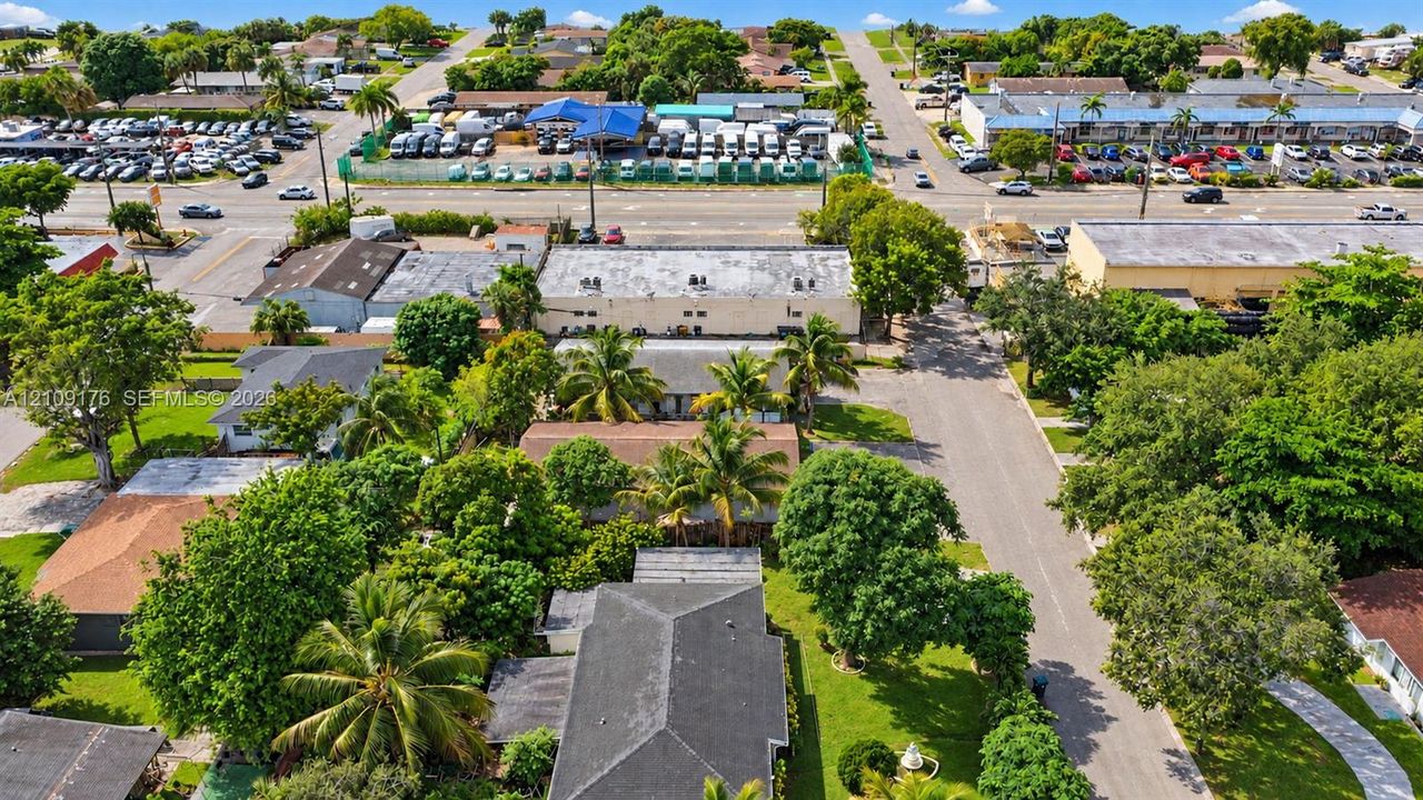 Aerial perspective of a residential property featuring a pitched shingle roof, mature landscaping, palm trees, and an asphalt driveway