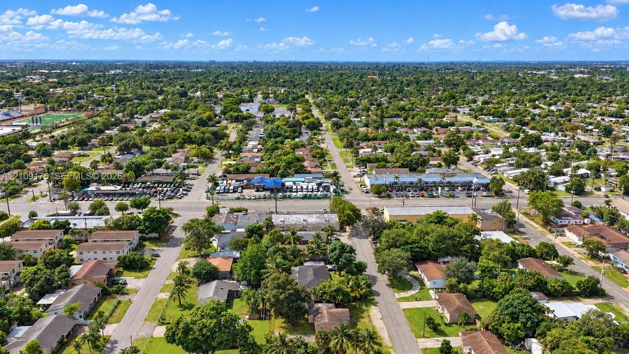 Aerial perspective of a suburban neighborhood featuring tree-lined streets, established residential lots, and proximity to local commercial thoroughfares