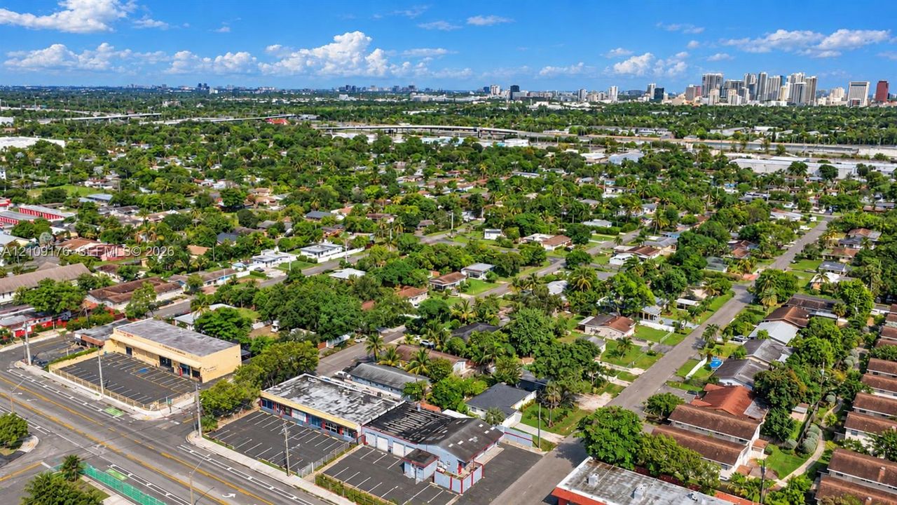 Aerial perspective featuring paved parking areas, surrounding lush canopy, and distant city skyline
