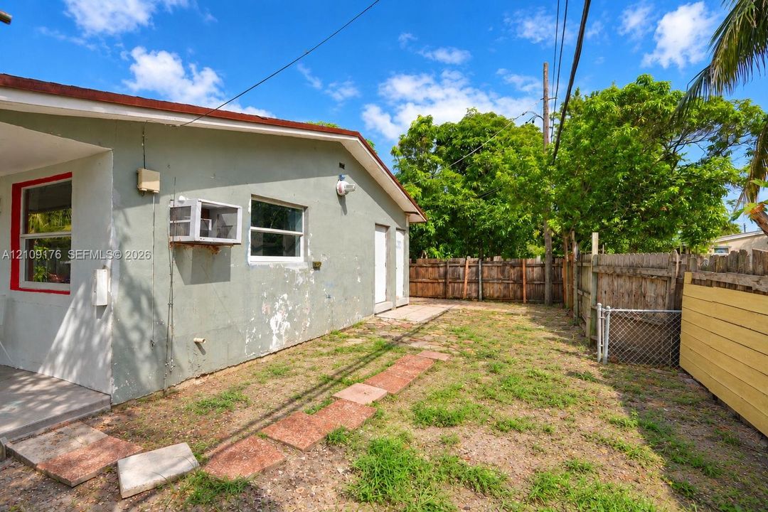 Exterior side yard featuring a concrete pathway, perimeter wood fencing, and mature trees