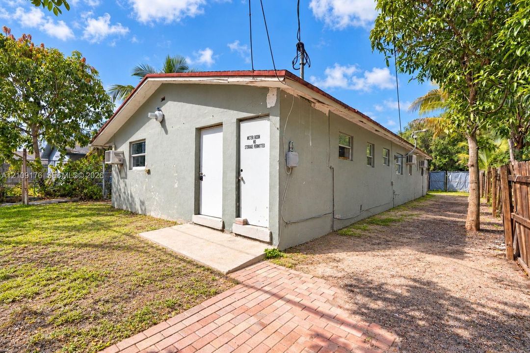 Exterior structure featuring a painted stucco finish, gable roofline, red brick paver walkway, and wooden privacy fencing