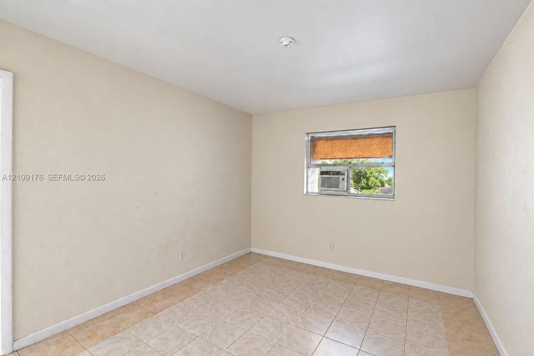 Interior space featuring neutral wall tones, large-format tile flooring, and a window with a built-in air conditioning unit