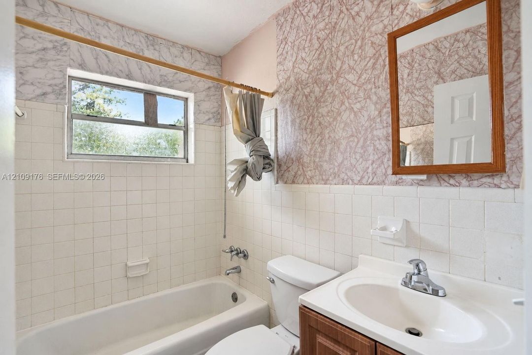 Full bathroom featuring a white porcelain tub with integrated shower, square-tile wall surround, vanity with an integrated sink, and a wall-mounted wood-frame mirror