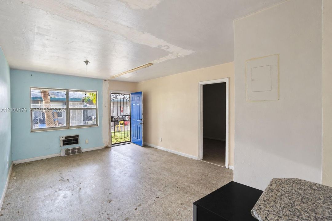 Interior space featuring terrazzo flooring, horizontal sliding windows, a wall-mounted air conditioning unit, and a metal security screen door