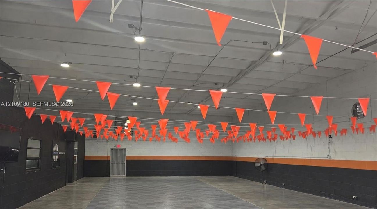 Open-concept commercial space featuring high ceilings with exposed trusses, recessed overhead lighting, polished concrete flooring, and painted masonry walls with dual-tone detailing
