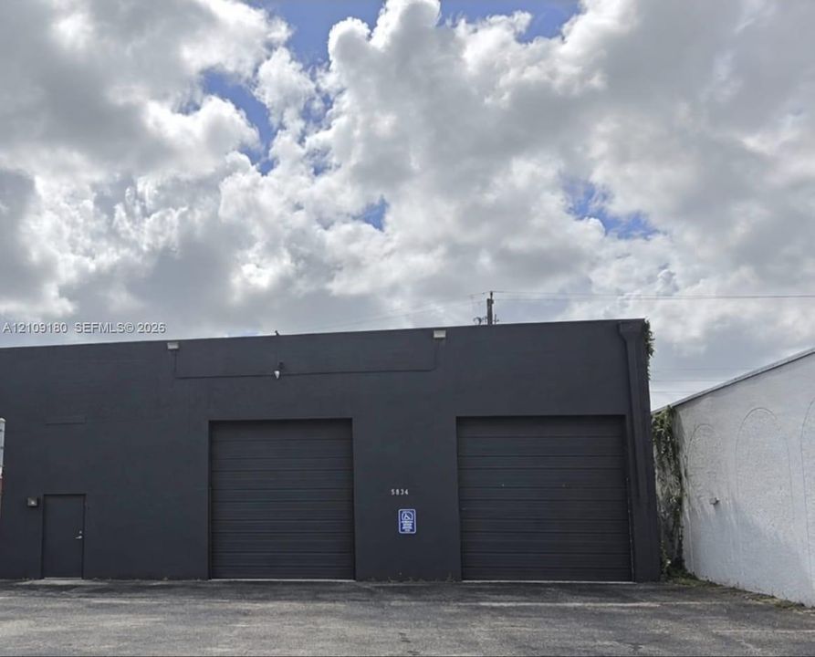 Exterior facade featuring a matte charcoal finish, two industrial-grade roll-up doors, a single entry door, and an asphalt parking area