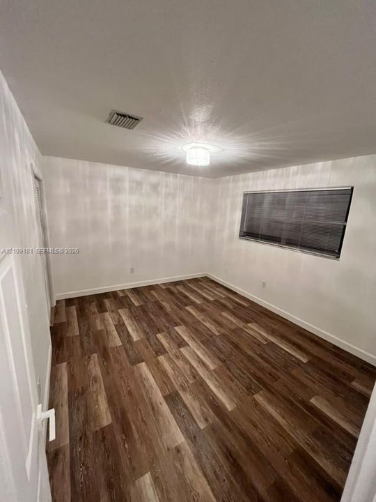 Interior room featuring wood-finish flooring, a flush-mount ceiling light fixture, and horizontal window blinds