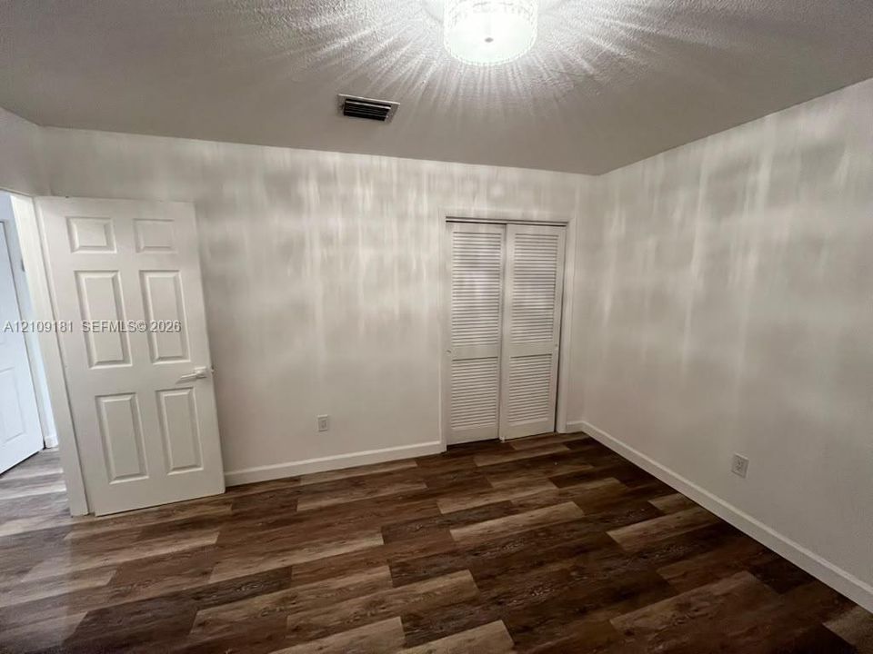 Interior space featuring wood-finish flooring, a six-panel door, louvered-style closet doors, and a flush-mount ceiling light fixture