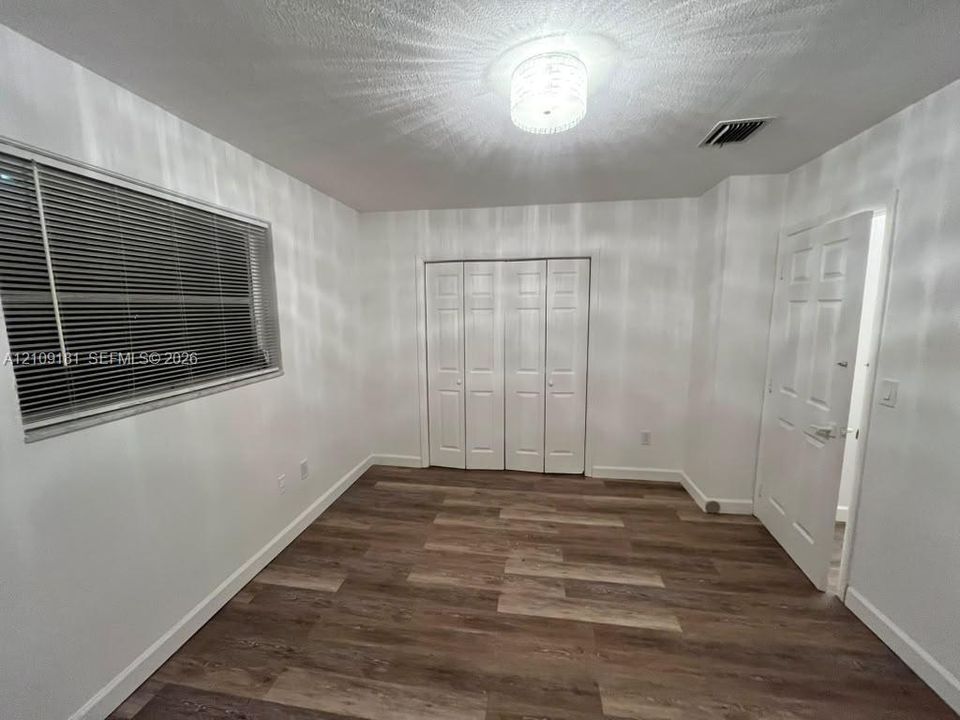 Room featuring wood-finish flooring, white paneled interior doors, a multi-panel closet, and a decorative flush-mount ceiling light fixture