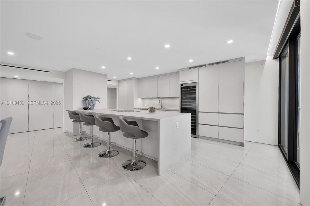 Kitchen featuring a waterfall island with stone countertop, flat-panel cabinetry, integrated wine refrigeration, recessed ceiling lighting, and polished stone flooring