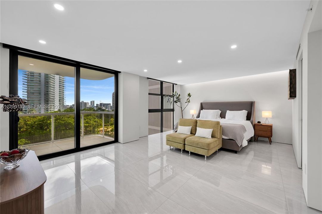 Floor-to-ceiling sliding glass doors, polished stone-finish flooring, recessed lighting, and a private balcony with metal railing