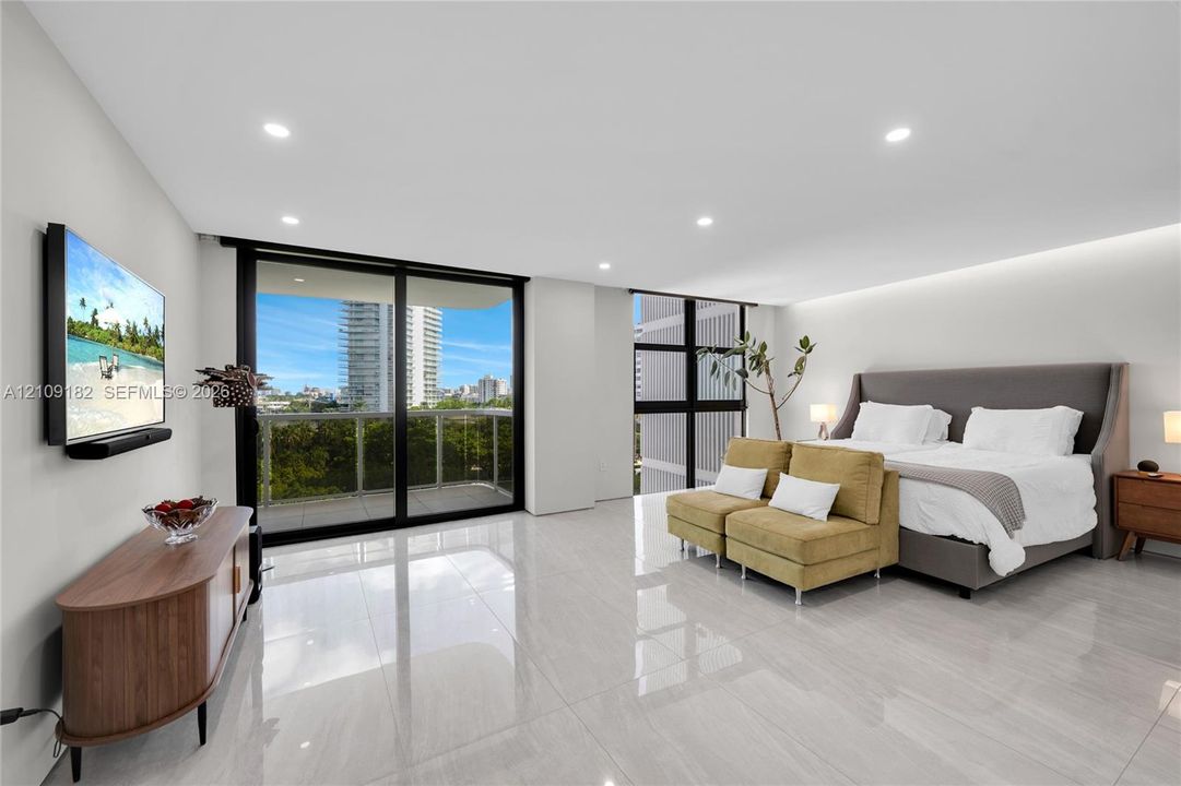 Spacious room featuring floor-to-ceiling glass sliding doors, polished tile flooring, recessed lighting, and a private balcony with glass railing