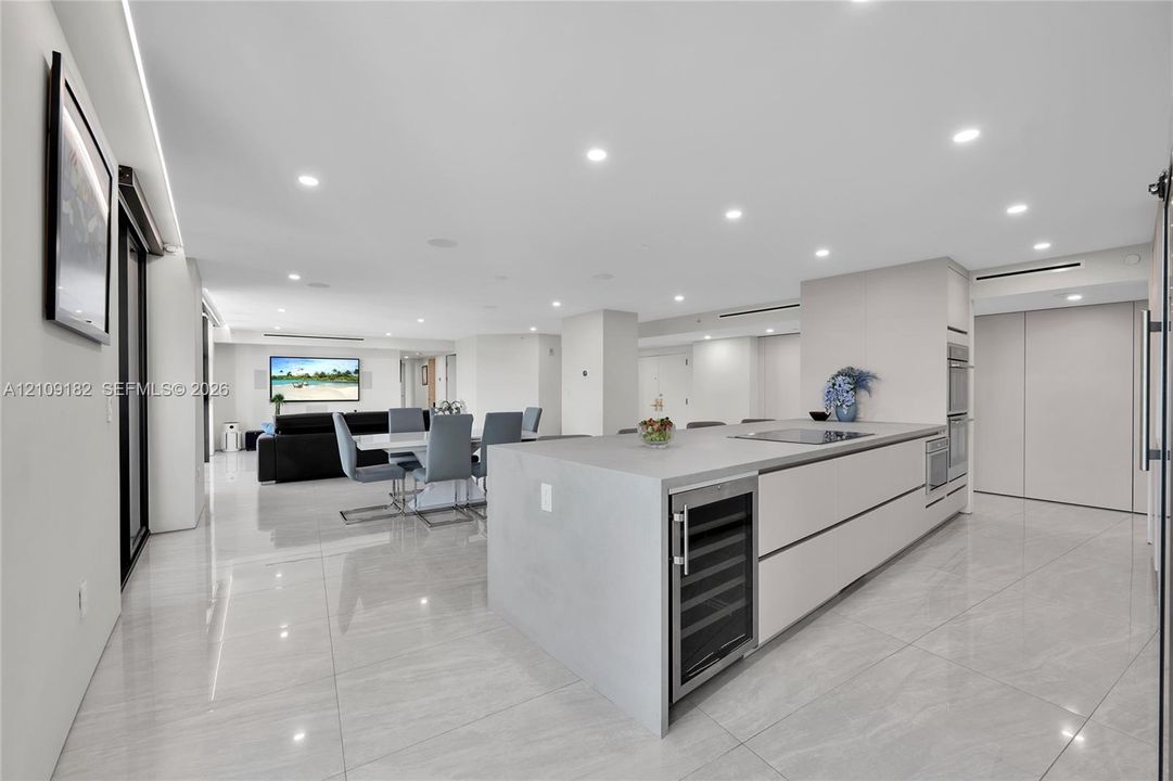Modern kitchen featuring large format tile flooring, flat-panel cabinetry, a central island with a built-in wine refrigerator, and recessed lighting