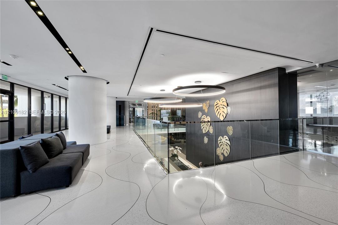 Polished flooring with integrated sweeping line patterns, custom circular overhead lighting, glass panel railing, and a dark accent wall featuring metallic botanical motifs