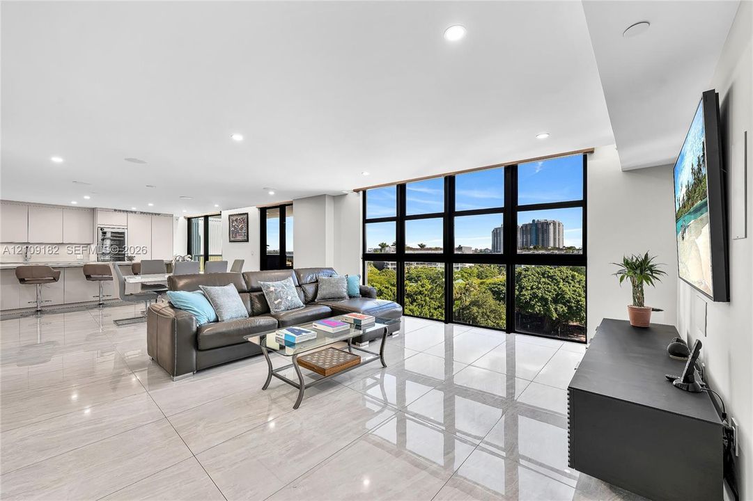 Floor-to-ceiling black-framed windows, large-format tile flooring, recessed ceiling lighting, and built-in kitchen cabinetry with stone countertops