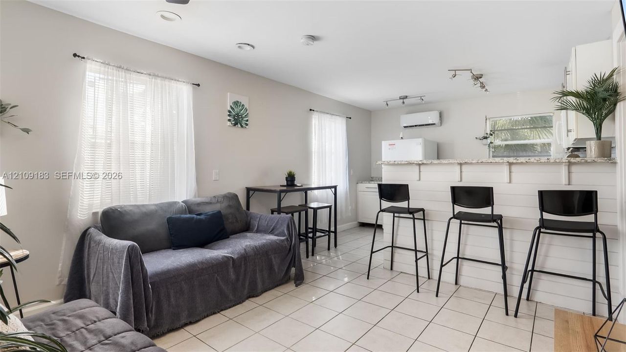 Neutral-toned interior featuring ceramic tile flooring, recessed lighting, and a breakfast bar with white horizontal paneling and a stone-surface countertop